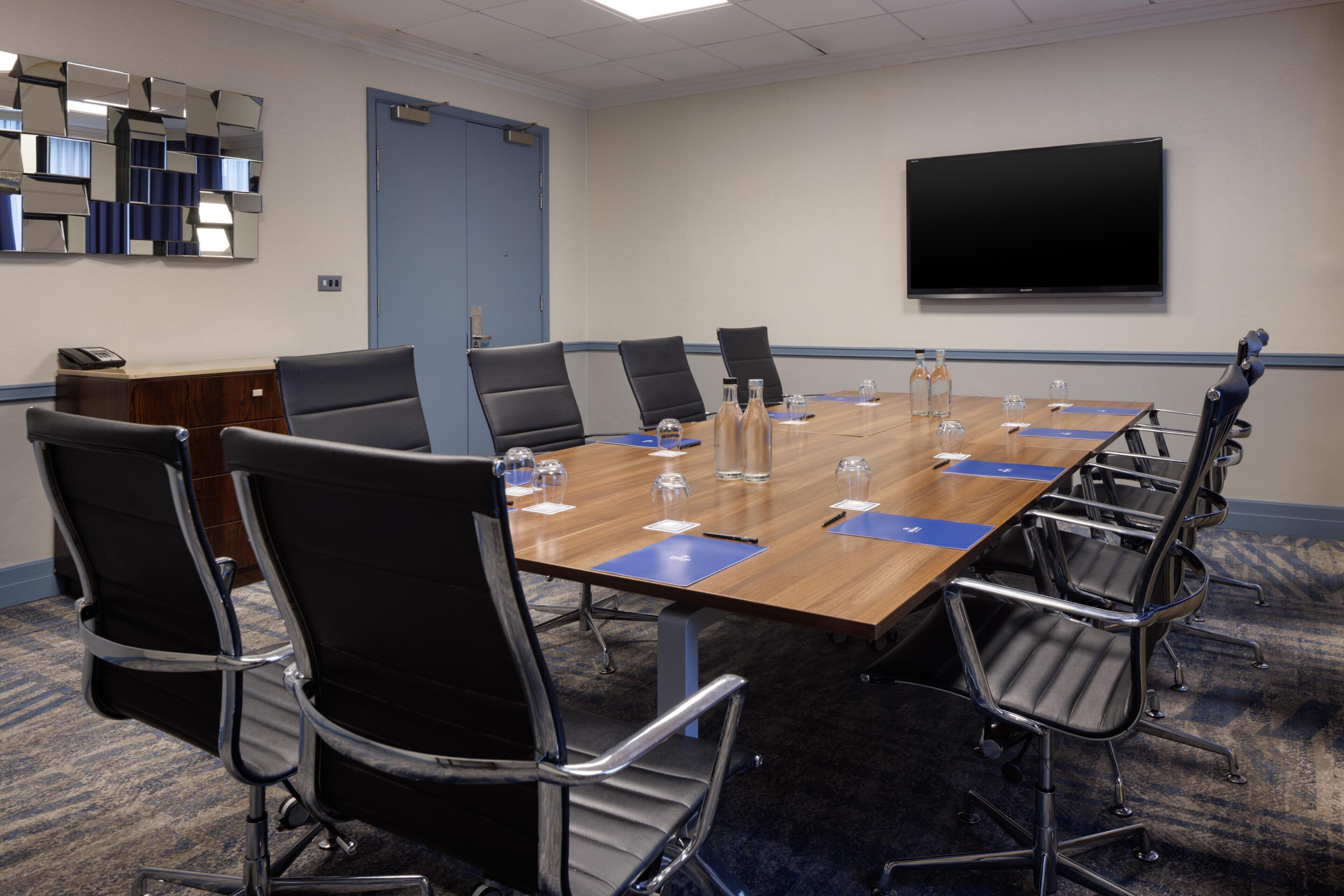 A conference room with a long table, chairs, a TV, and a door.