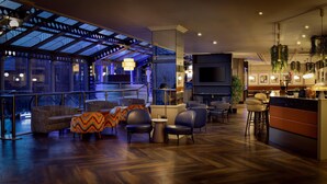 A modern lounge area with seating, a bar, and a large TV screen. - Hilton Leeds City Hotel (Leeds)