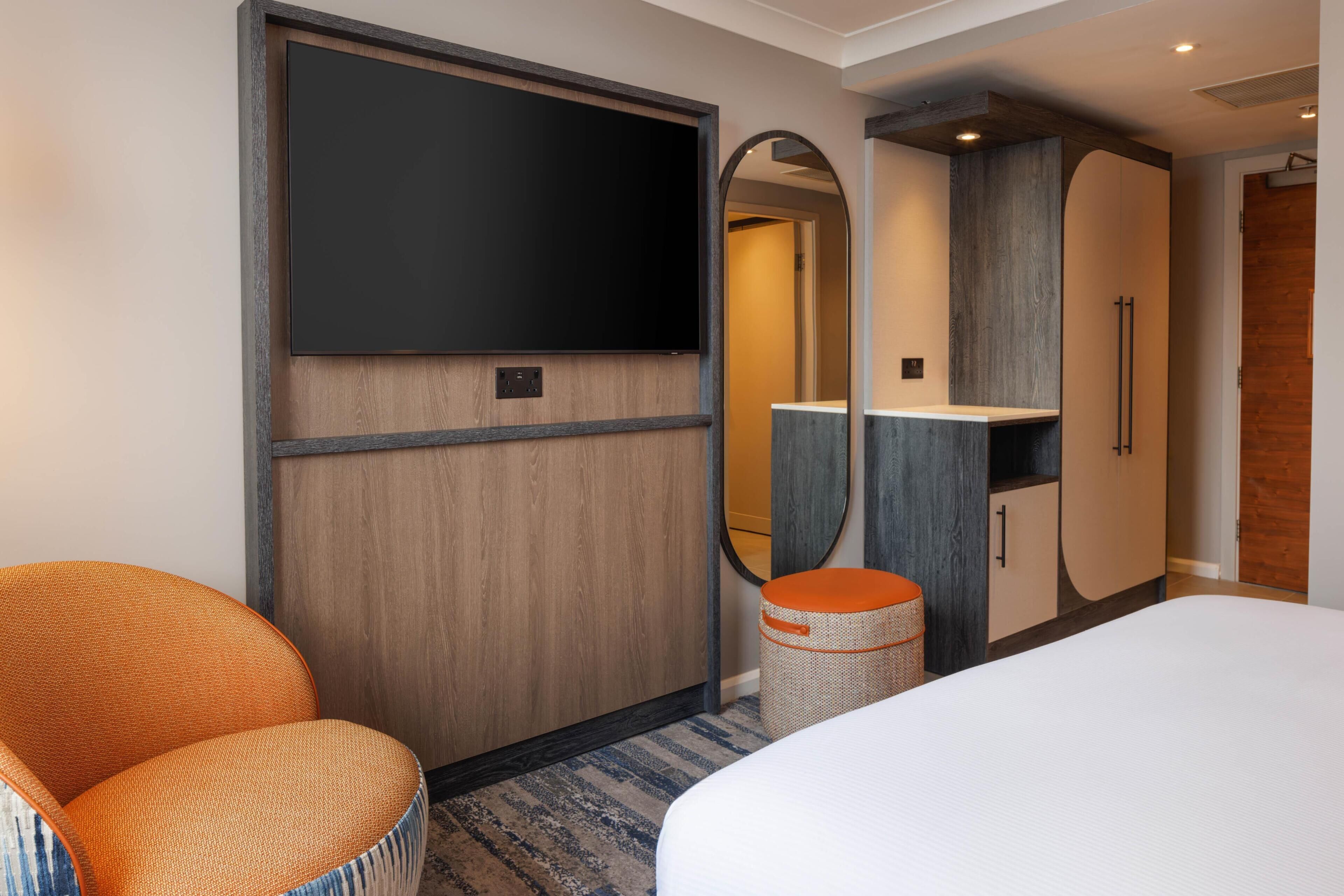 Une chambre d’hôtel avec un lit, une chaise, une armoire, un miroir et un téléviseur.