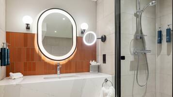 A modern bathroom with a large mirror, a shower, and a vanity with a sink.