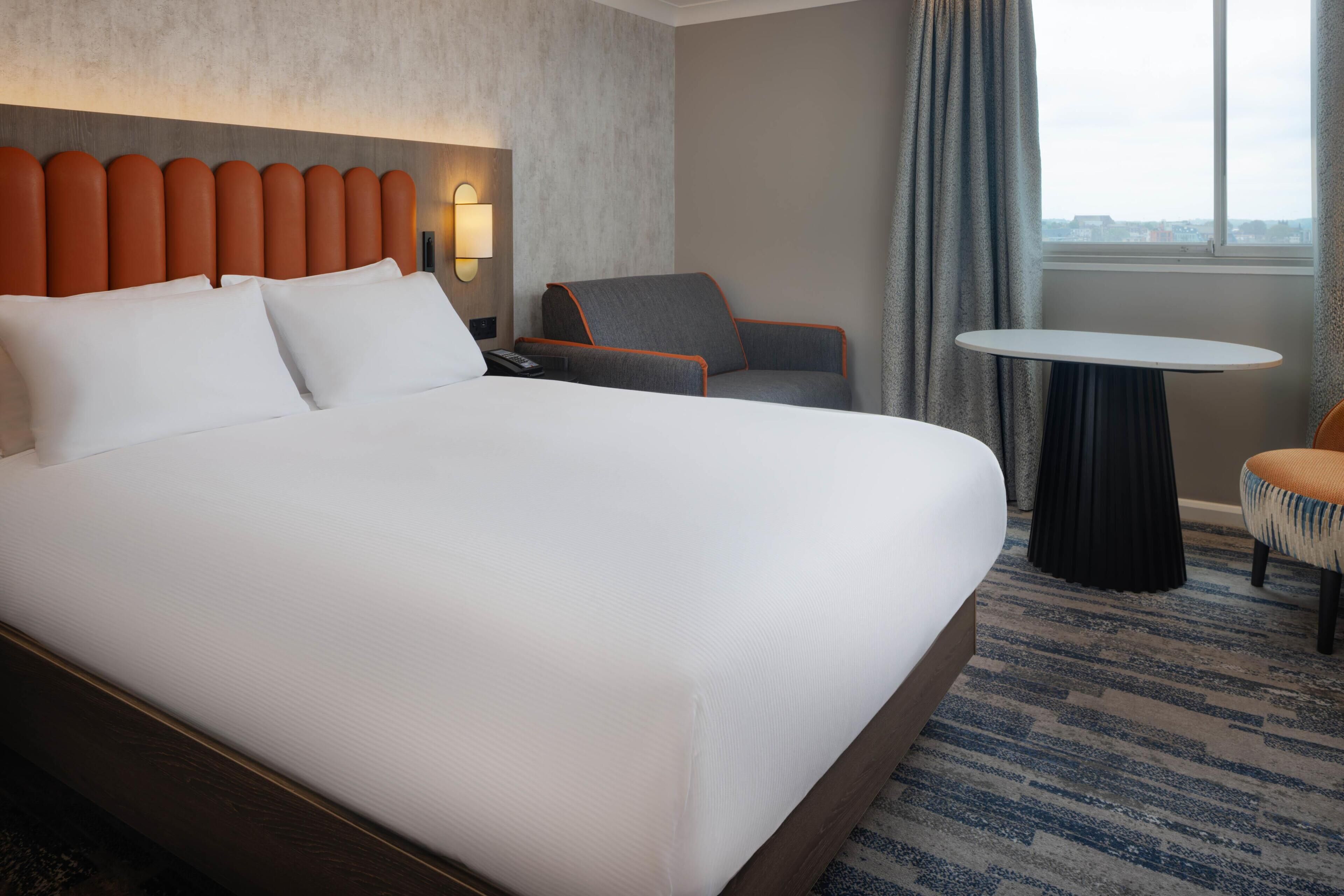 Une chambre d’hôtel avec un grand lit, une chaise, une petite table et une vue sur la ville par la fenêtre.
