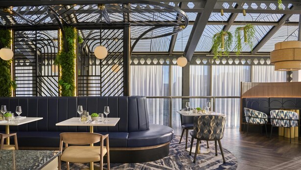 A modern restaurant with a curved seating area, tables, and hanging plants. - Hilton Leeds City Hotel (Leeds)