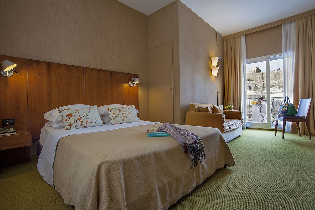 Une chambre d’hôtel avec un grand lit, un canapé, un fauteuil et un balcon avec vue.