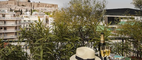 A table with a hat, book, glasses, a bottle, and a glass of wine, overlooking a cityscape with ancient ruins.