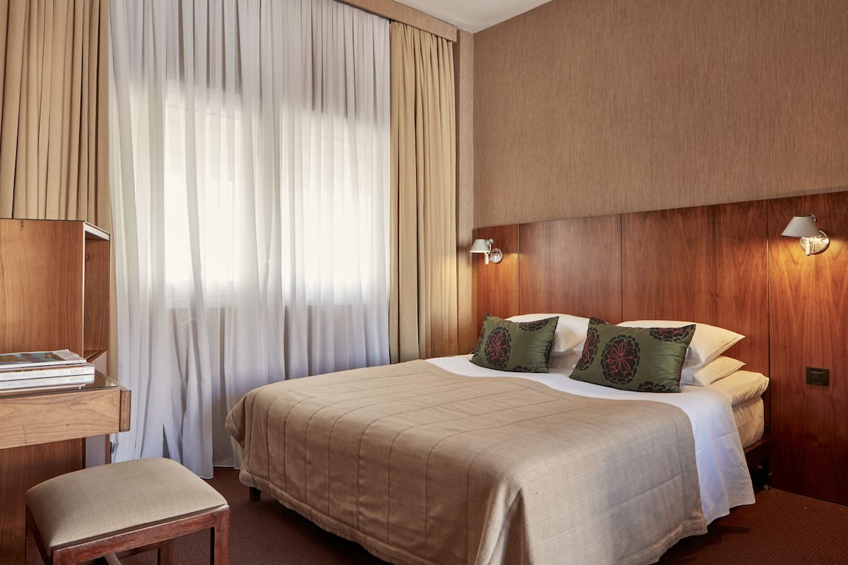 Une chambre d’hôtel avec un grand lit, une table de chevet en bois, un bureau et une chaise.