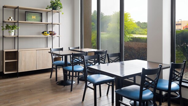 A modern dining area with a large window, wooden flooring, and a built-in bookshelf with plants.