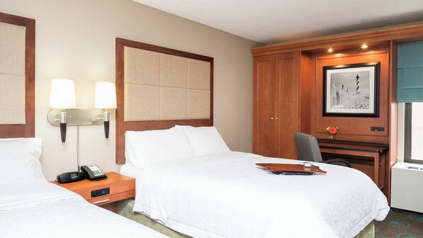 A hotel room with two beds, a desk with a chair, a telephone, and a framed picture on the wall.