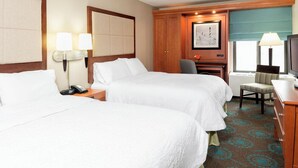 A hotel room with two beds, a desk, a chair, a telephone, and a television.