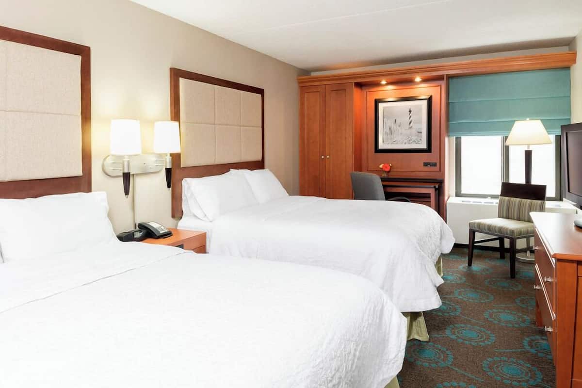 A hotel room with two beds, a desk, a chair, a telephone, and a television.