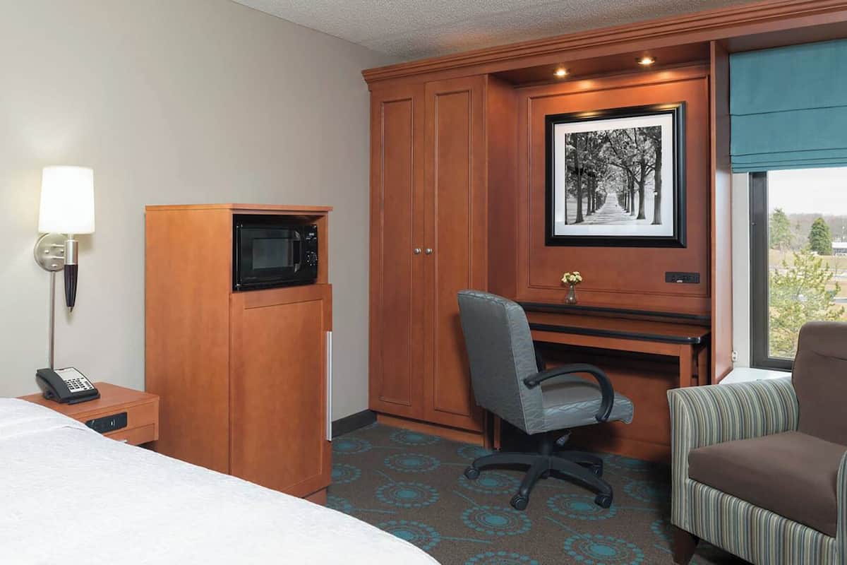 A hotel room with a bed, a desk with a computer, a telephone, a microwave, and a chair.