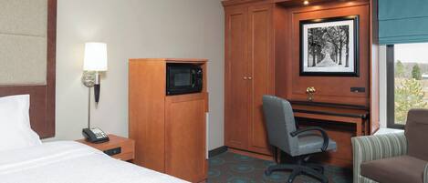 A hotel room with a bed, a desk with a computer, a telephone, a microwave, and a chair.