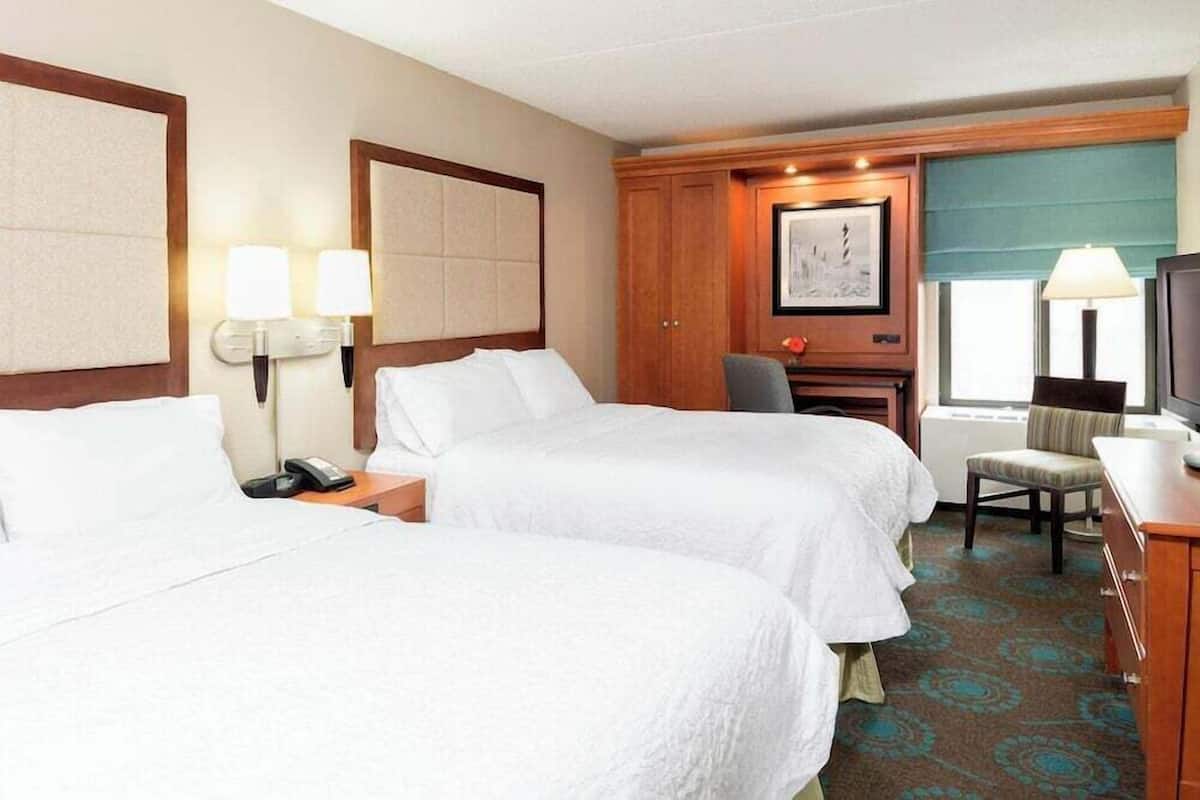 A hotel room with two beds, a desk, a chair, a TV, and a window with a view.