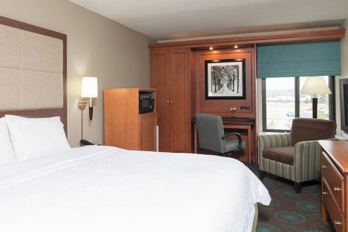 A hotel room with a large bed, a desk with a computer, a chair, a television, and a window with a view.
