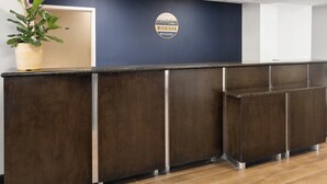 A reception desk with a dark wood finish, a potted plant on the left, and a logo on the wall.