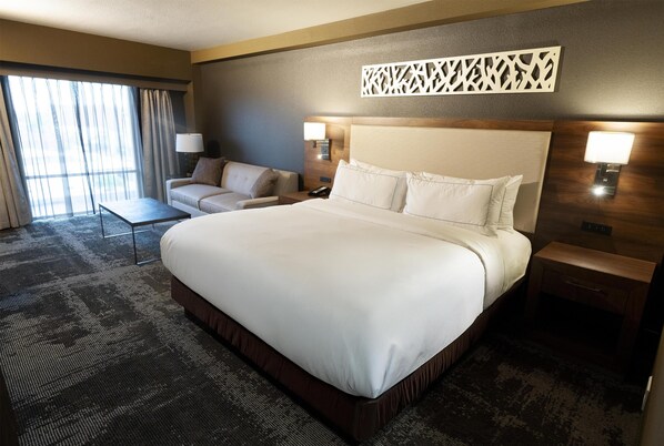 A hotel room with a large bed, a sofa, a desk, and a view of the outdoors through the window.