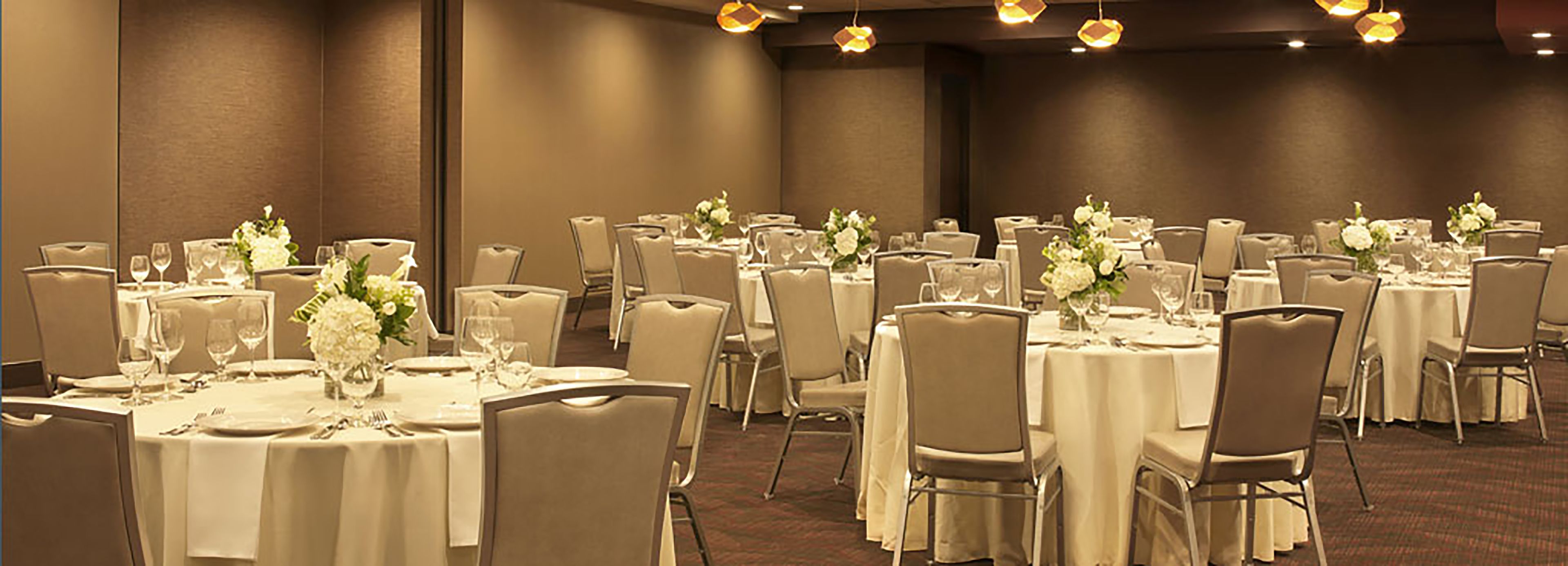 A banquet hall with round tables, chairs, and floral centerpieces.
