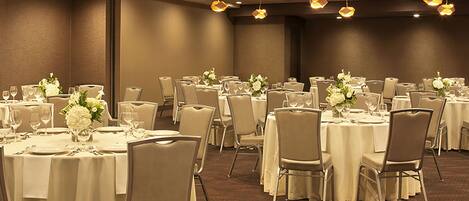 A banquet hall with round tables, chairs, and floral centerpieces.