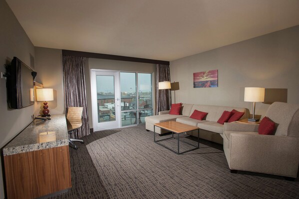 A hotel room with a sofa, armchairs, a coffee table, a desk with a lamp, and a large window with curtains. - The Broadway Columbia - a DoubleTree by Hilton (Columbia)