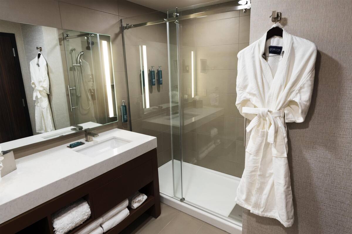 A modern bathroom with a glass-enclosed shower, a large mirror, and a white robe hanging on the wall.