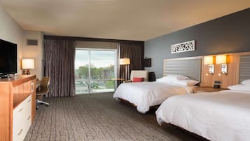 A hotel room with two beds, a TV, a desk, and a view of the city.