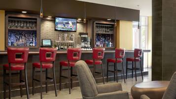 A bar area with red bar stools, a television mounted above the bar, and a variety of bottles and glasses on shelves.