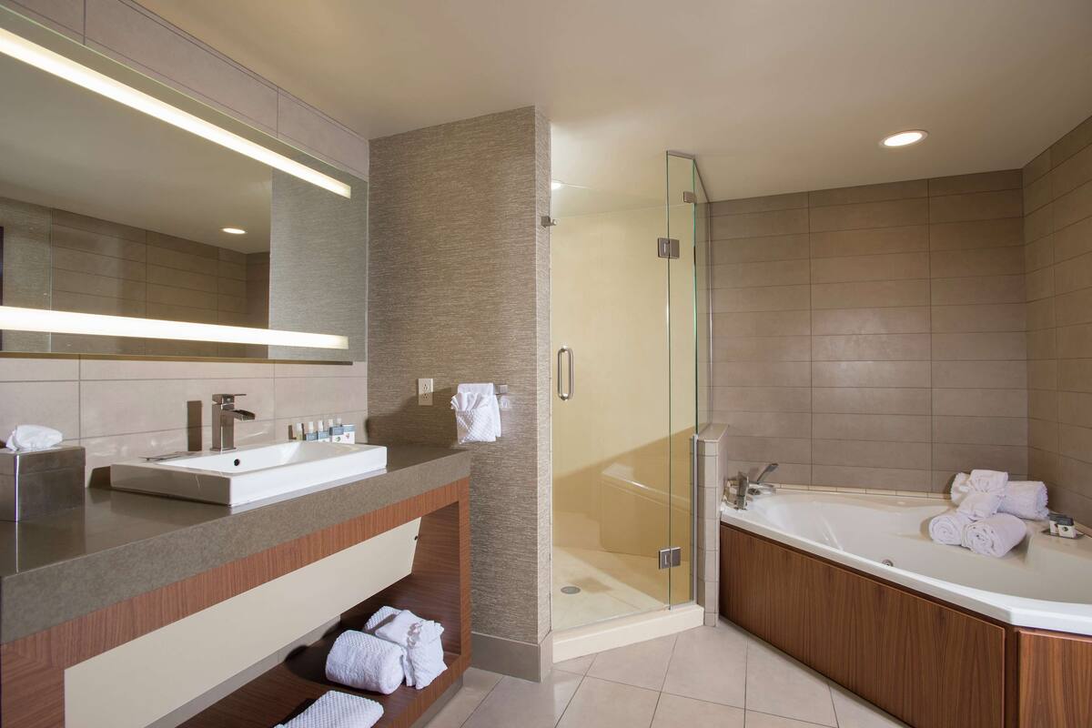 A modern bathroom with a large mirror, a sink, a shower enclosure, and a bathtub.
