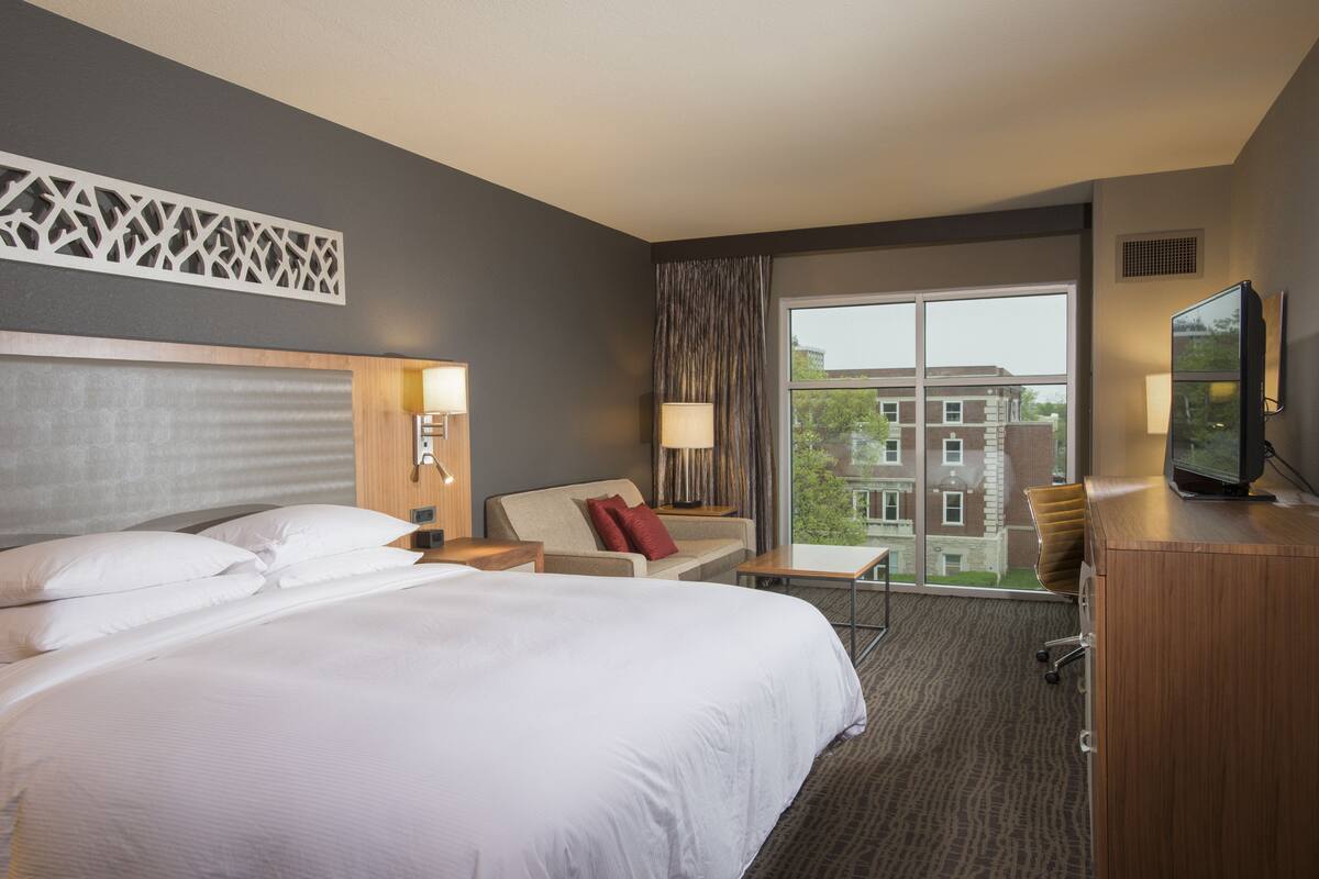 A hotel room with a large bed, a sofa, a desk, and a television.