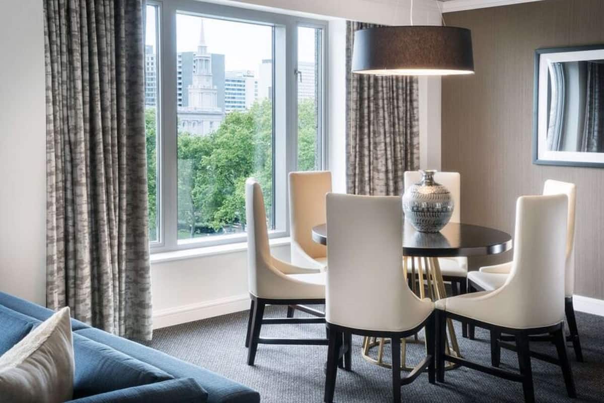 A hotel room with a dining area featuring a round table, four chairs, and a vase.