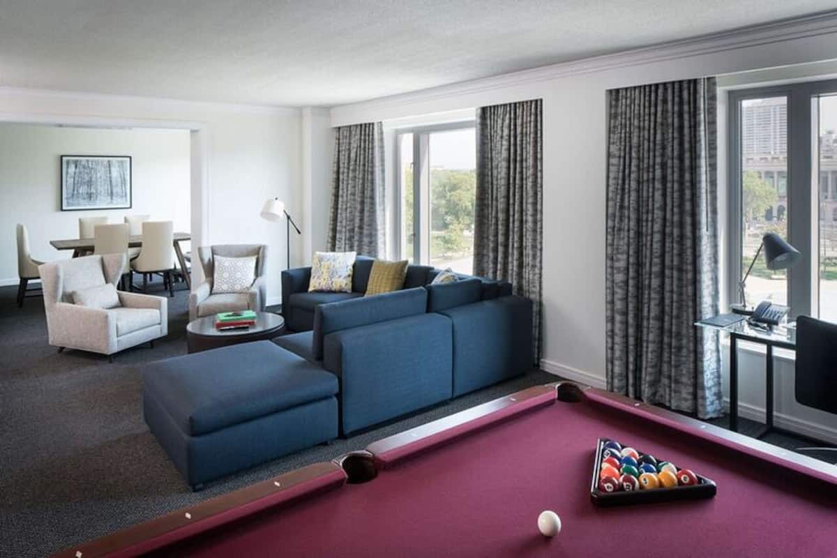A modern living room with a pool table, a blue sofa, and a dining area with chairs and a table.