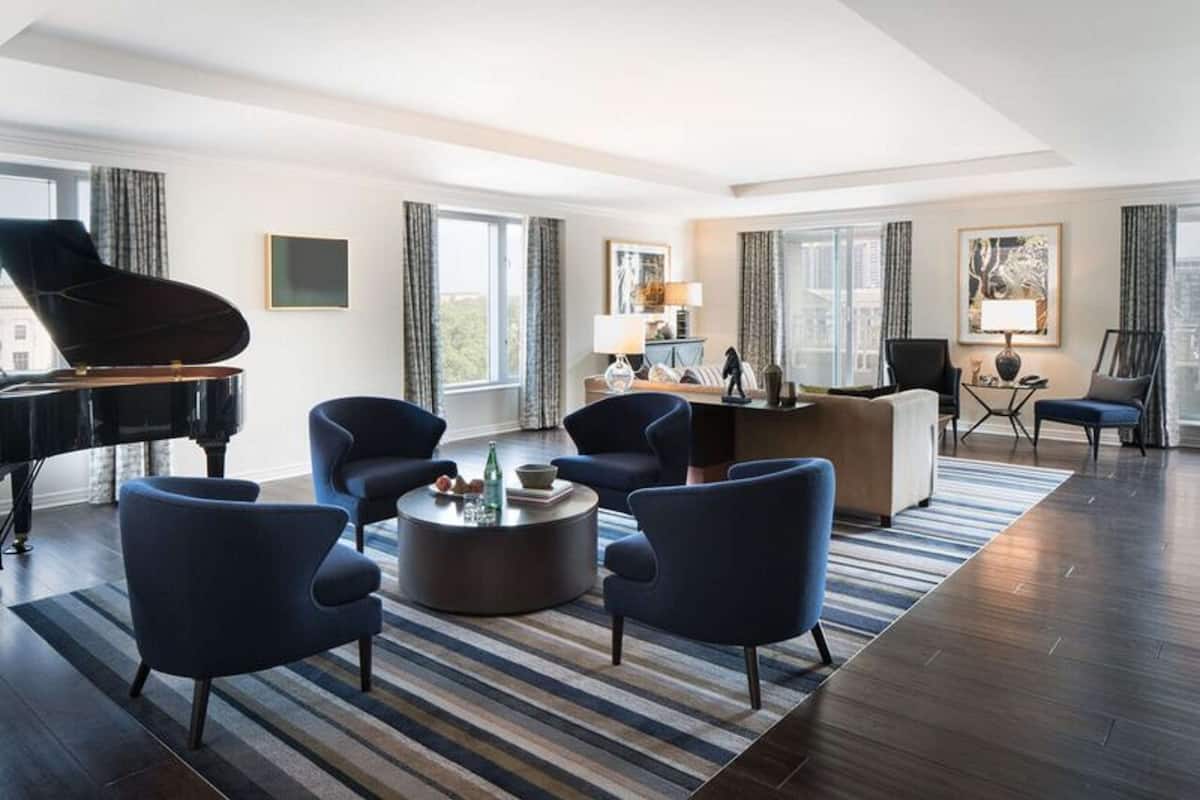 A modern living room with a grand piano, dark blue armchairs, a round coffee table, and a striped rug.