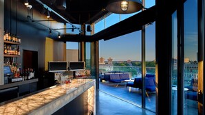 A modern bar area with a marble countertop, multiple TVs, and a city view through large windows. - The Logan Philadelphia, Curio Collection by Hilton (Philadelphia)
