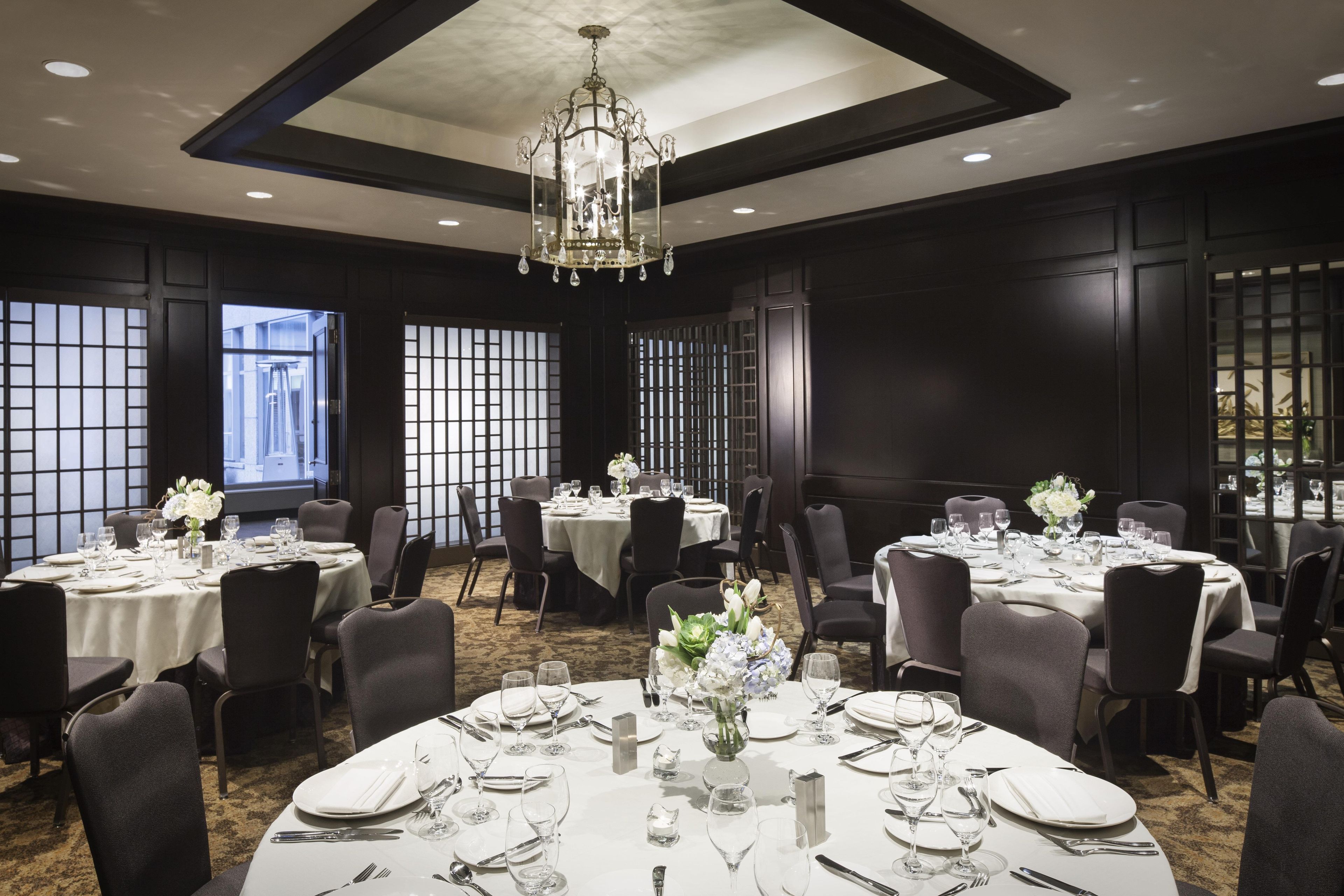 Un comedor formal con varias mesas dispuestas para el servicio, un candelabro y ventanas amplias con vistas.