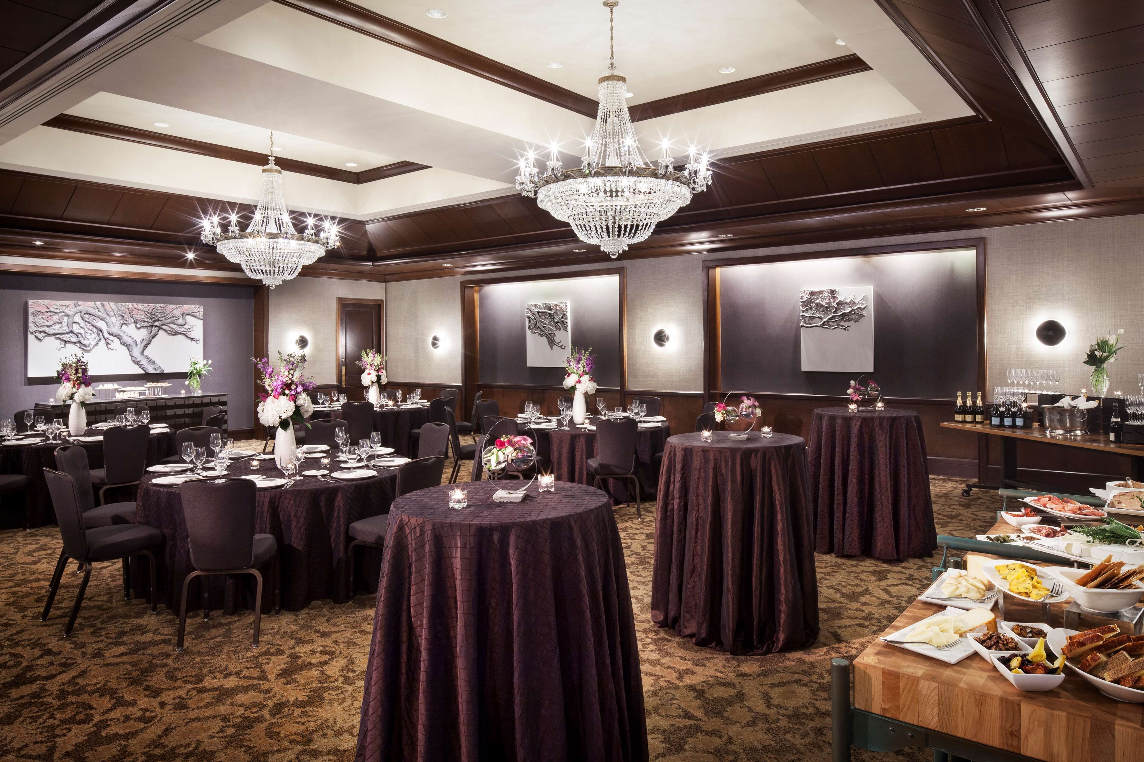 Un salón de banquetes con mesas redondas, cortinas oscuras, candelabros y obras de arte en las paredes.