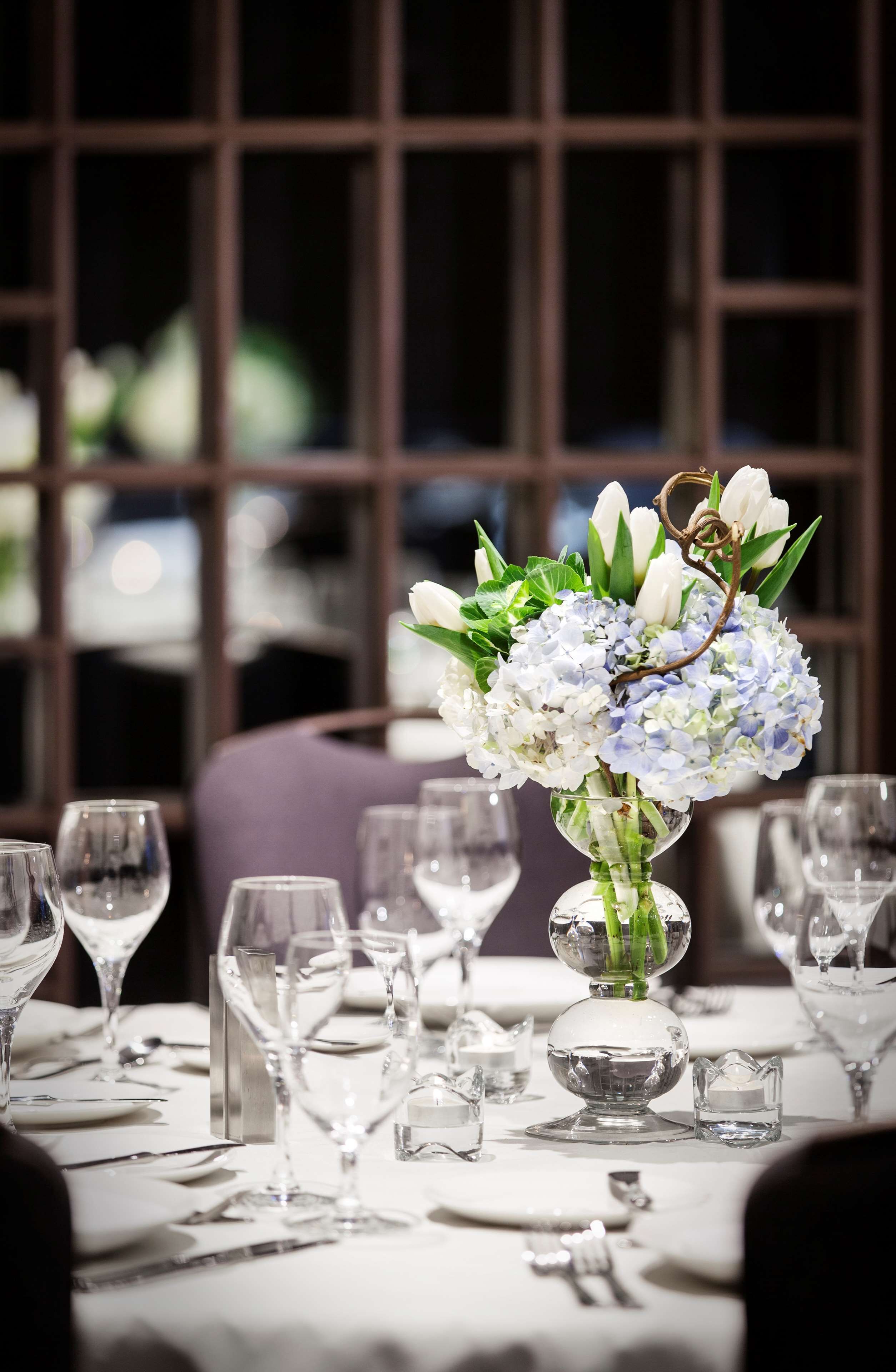 A dining table set with clear glassware and a centerpiece of white and blue flowers.