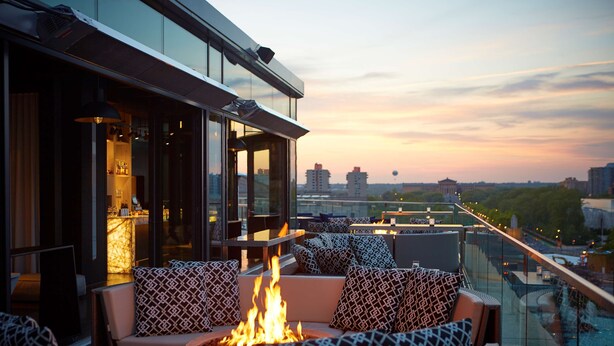 A rooftop lounge with a fire feature, seating with patterned cushions, and a city view at sunset. - The Logan Philadelphia, Curio Collection by Hilton (Philadelphia)