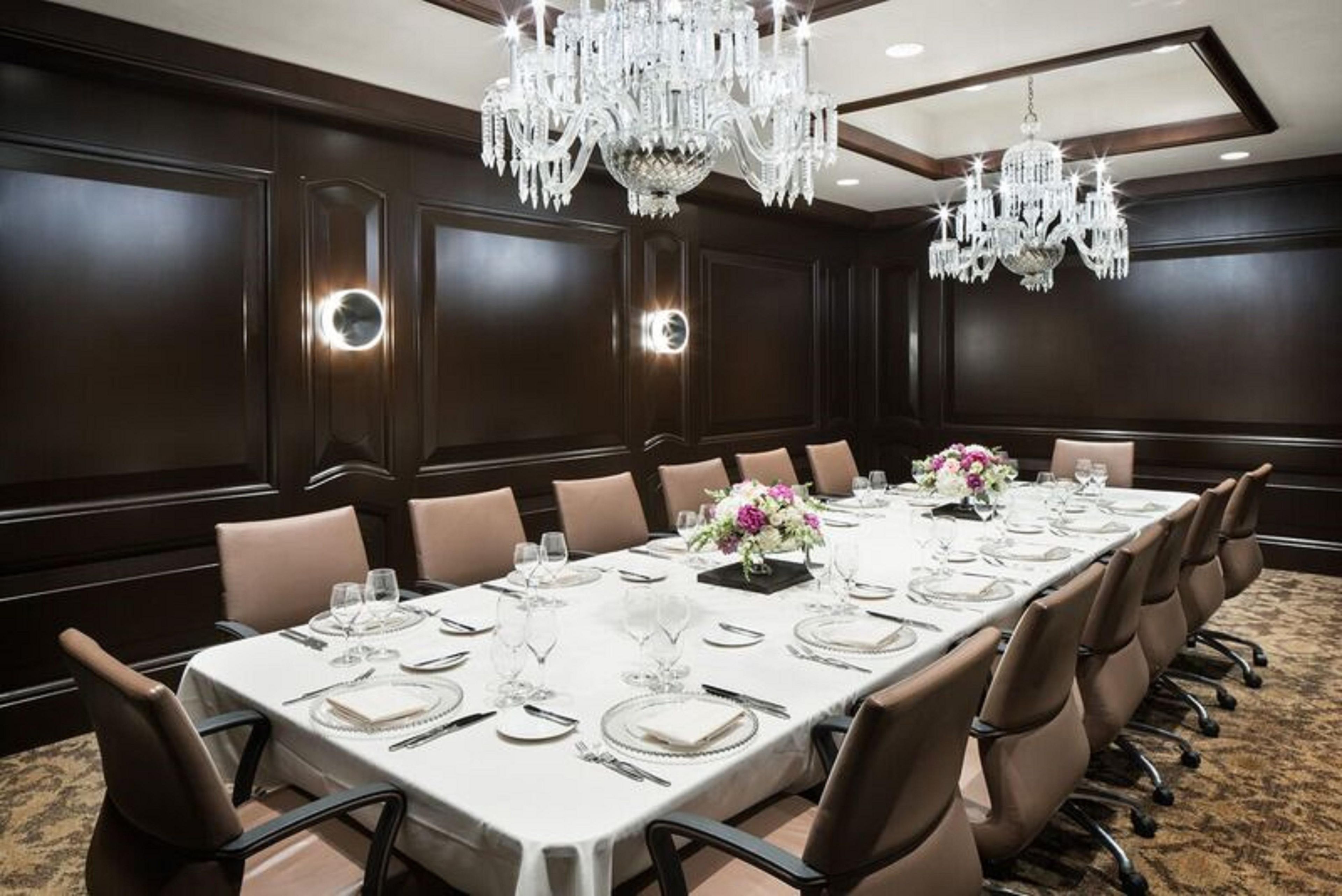A conference room with a long table set for a meeting, surrounded by chairs, with chandeliers and wall sconces providing lighting.