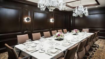 A conference room with a long table set for a meeting, surrounded by chairs, with chandeliers and wall sconces providing lighting.