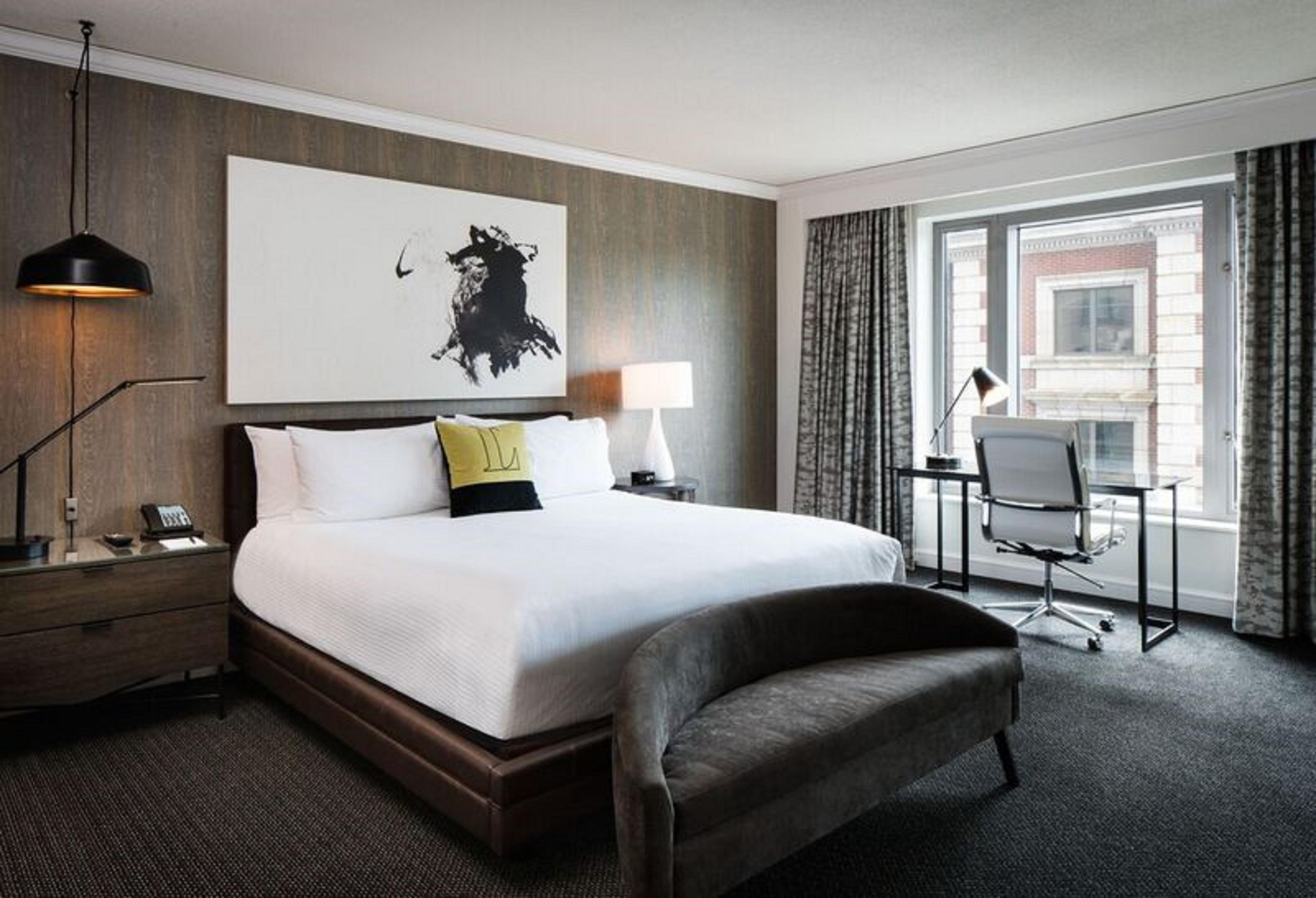 Ein Hotelzimmer mit einem großen Bett, einem Schreibtisch, einem Stuhl, einer Lampe und einem fenster mit Vorhängen.