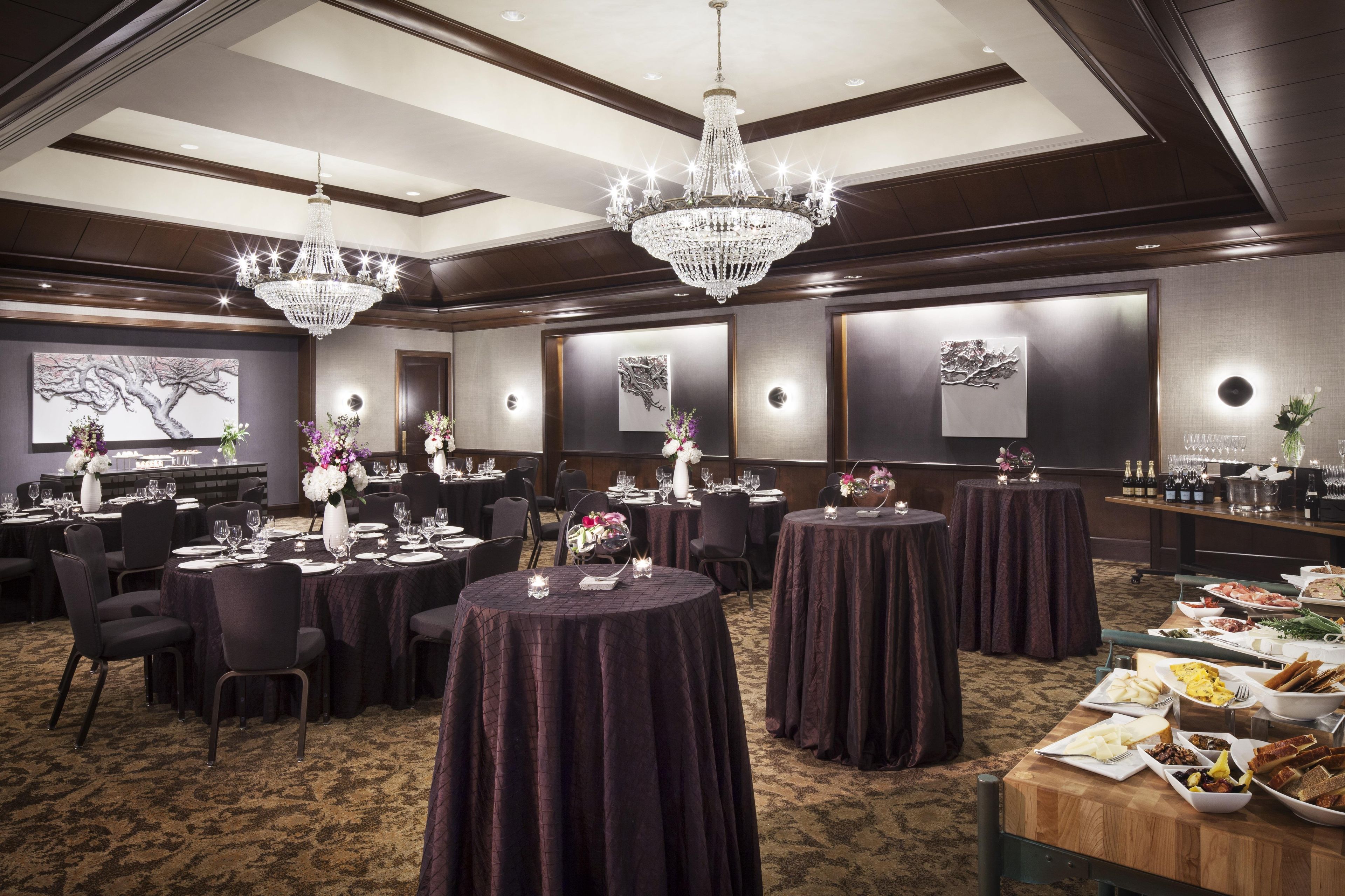 A banquet hall with round tables, chandeliers, and wall-mounted light fixtures.