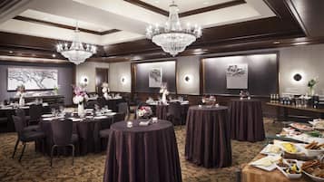 A banquet hall with round tables, chandeliers, and wall-mounted light fixtures.