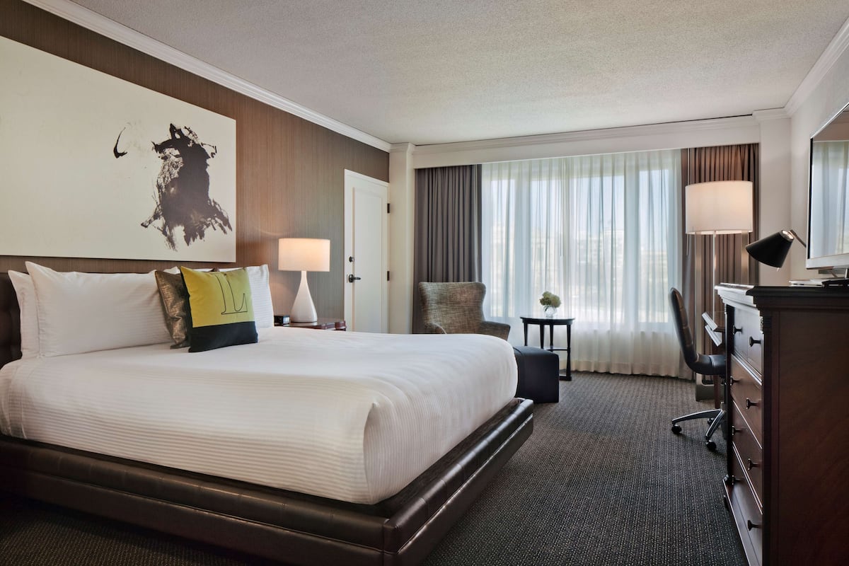 A hotel room with a large bed, a desk, a chair, and a window with curtains.