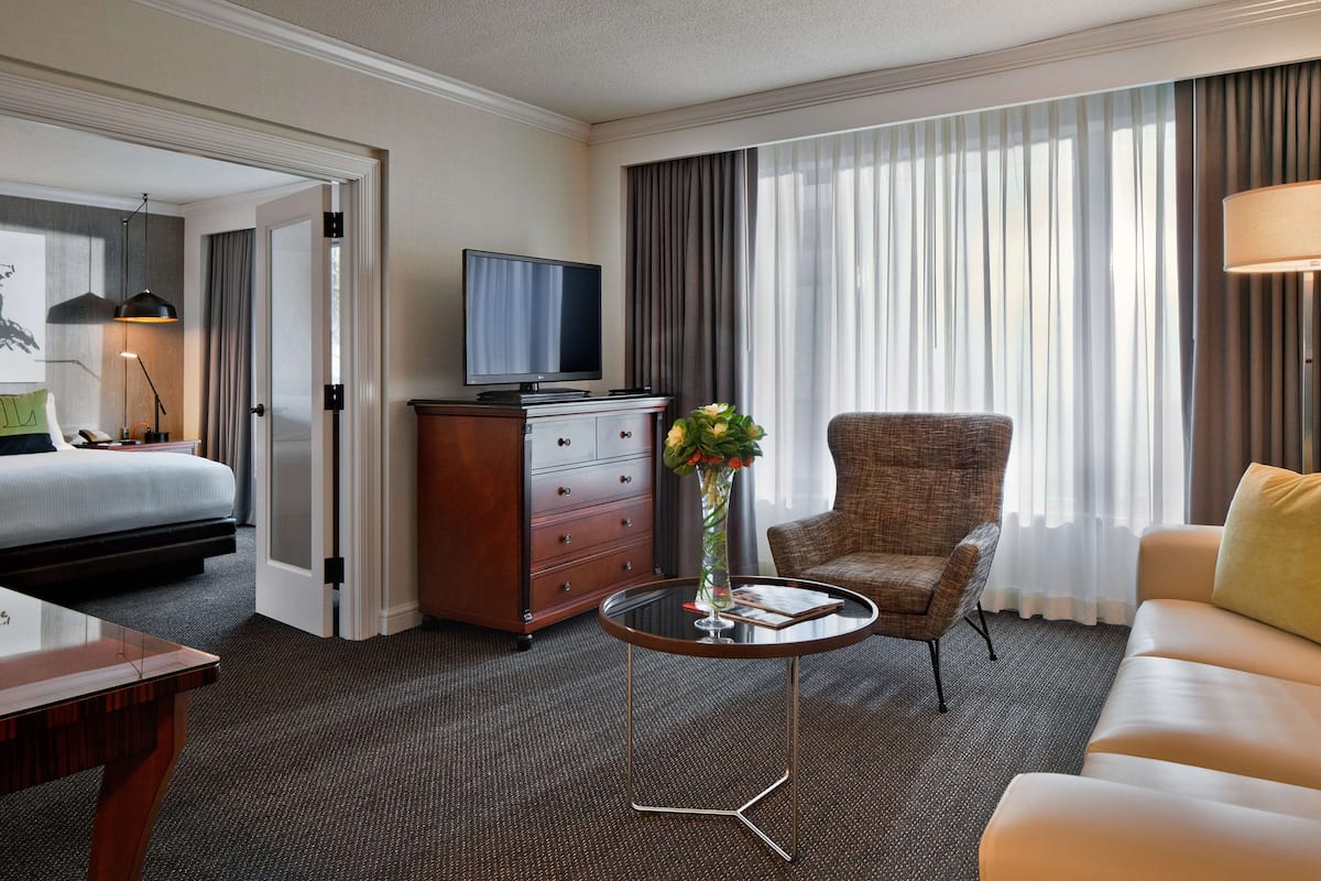 A hotel room with a bed, a television, a desk, a chair, a sofa, and a vase with flowers.