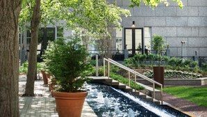 A landscaped area with a water feature, potted plants, and a building in the background. - The Logan Philadelphia, Curio Collection by Hilton (Philadelphia)