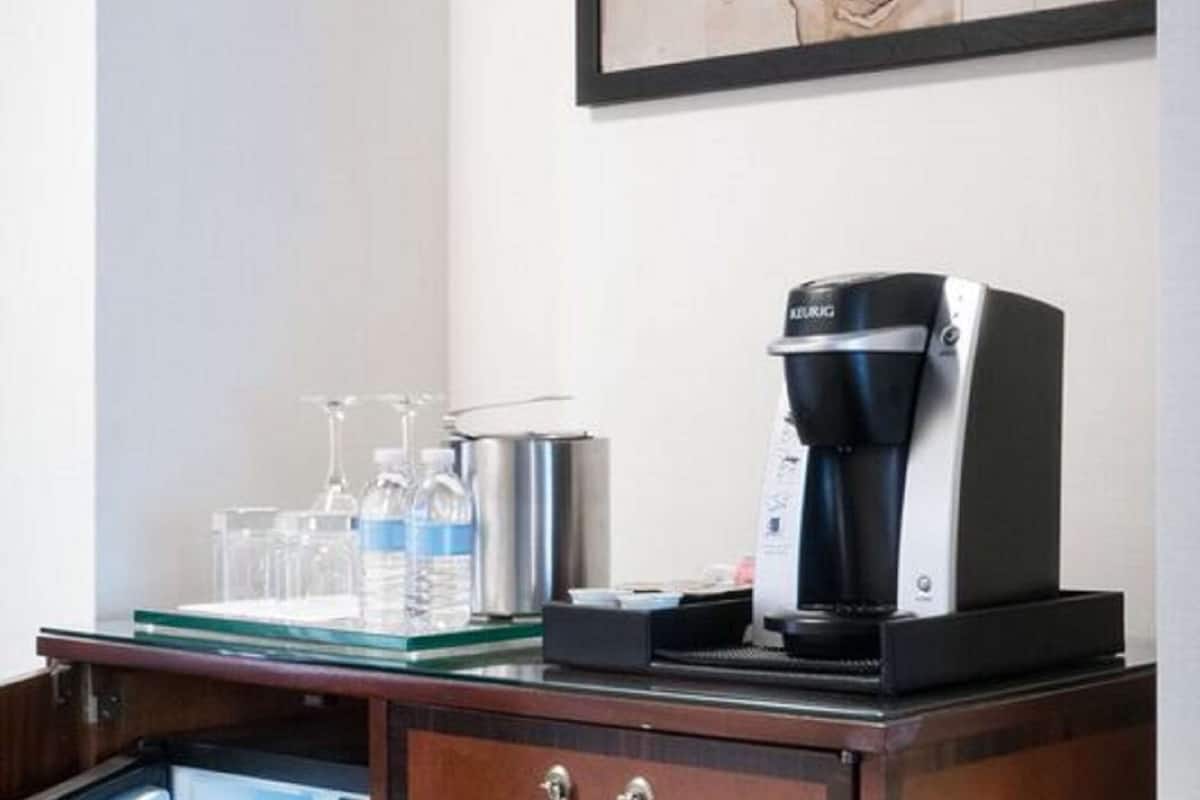 A minibar with a coffee maker, water bottles, and glasses on a wooden cabinet.