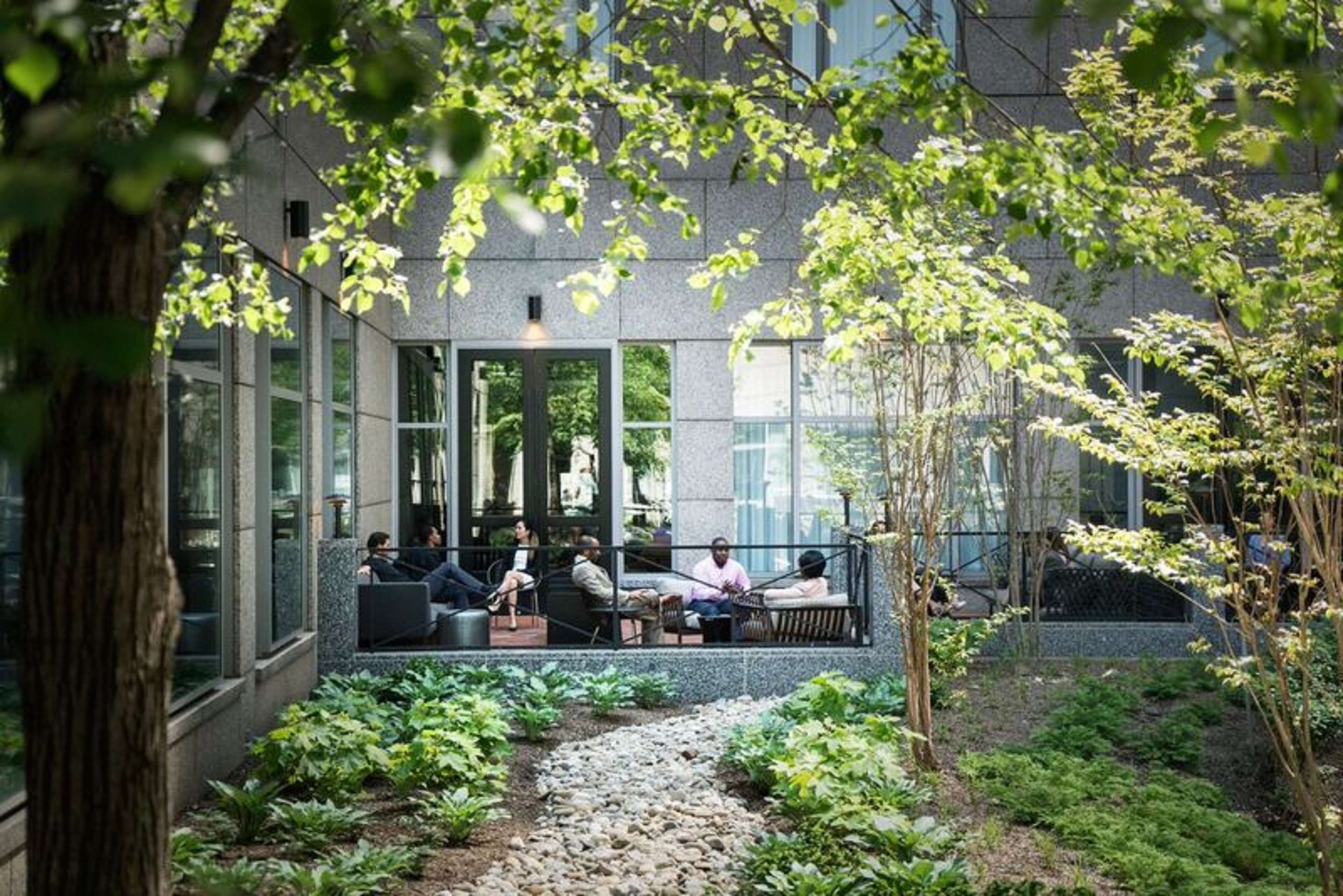 An outdoor seating area with tables and chairs, surrounded by greenery and a stone pathway.