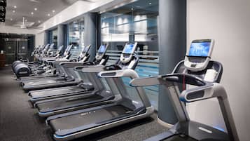 A row of treadmills in a modern gym with large windows and a ceiling fan.