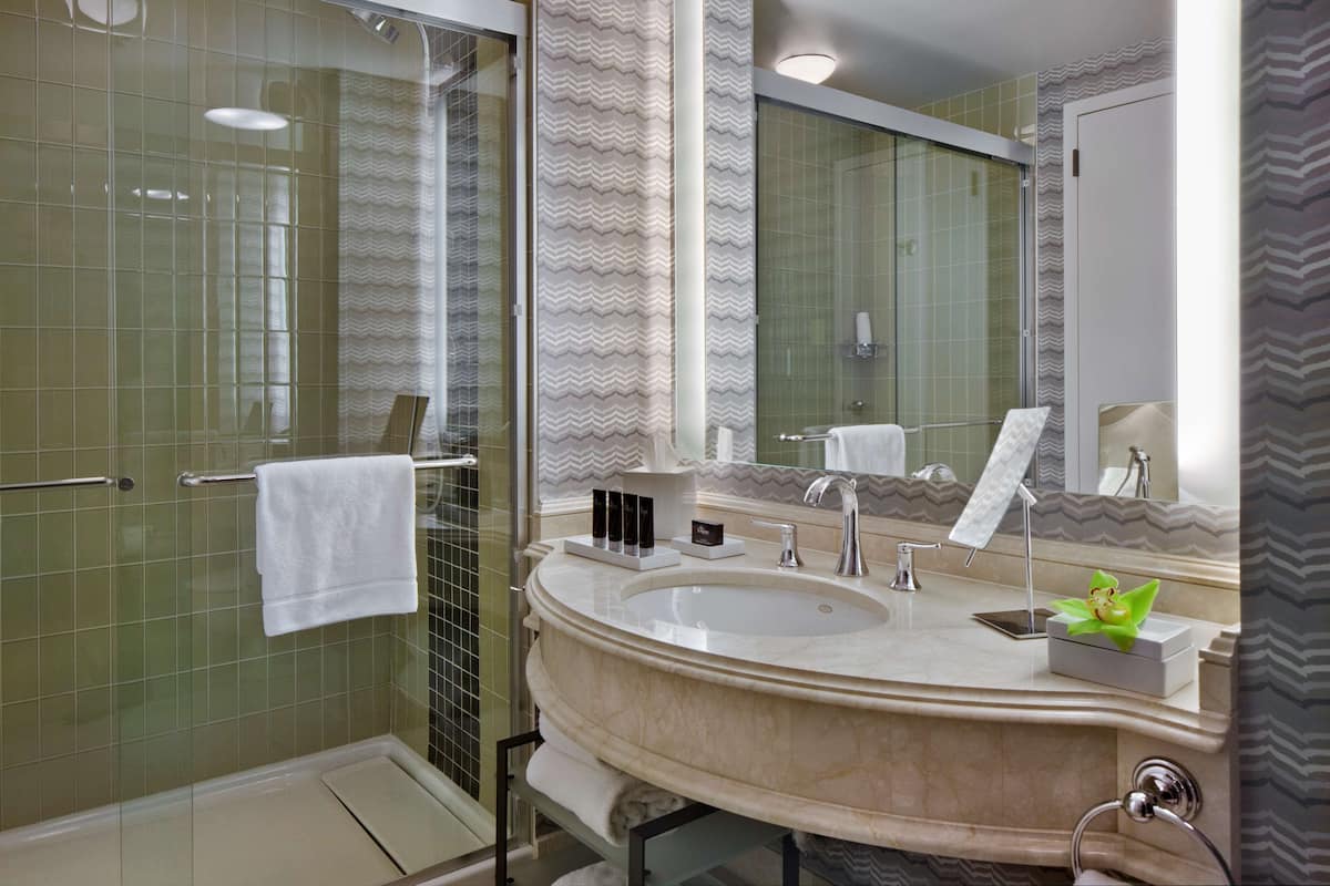 A bathroom with a glass shower enclosure, a large sink with a mirror, and a towel rack.