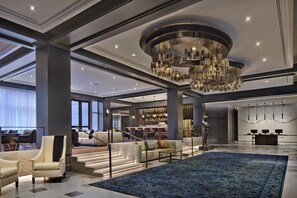 Um hall amplo com um lustre imponente, área de bar e espaço de estar com carpete azul.