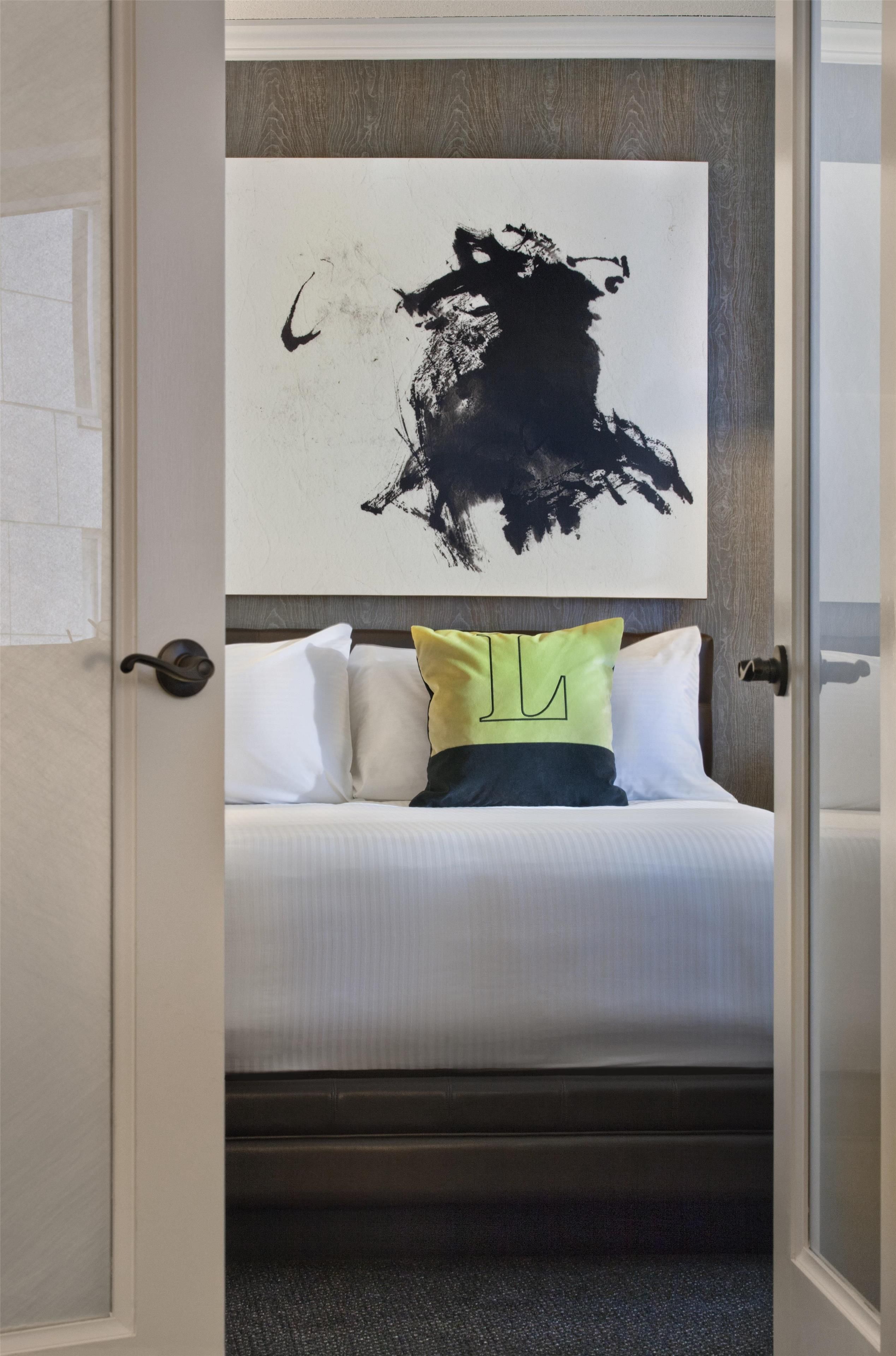 Una camera d'albergo con un letto, un quadro astratto di grandi dimensioni appeso al muro e una porta con pomello.