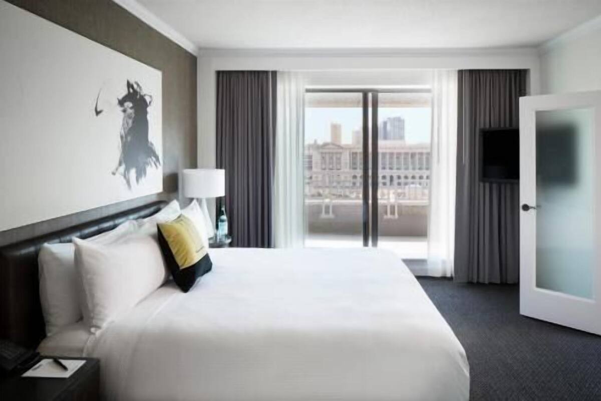 A hotel room with a large bed, a desk with a lamp, a television, and a view of the city.